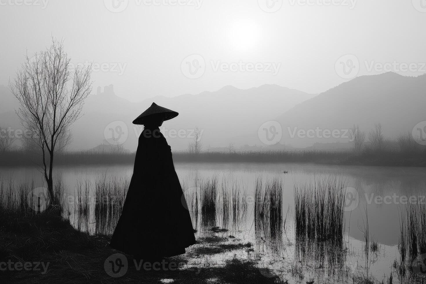 Silhouette of a figure by the calm water at dawn in a misty landscape photo