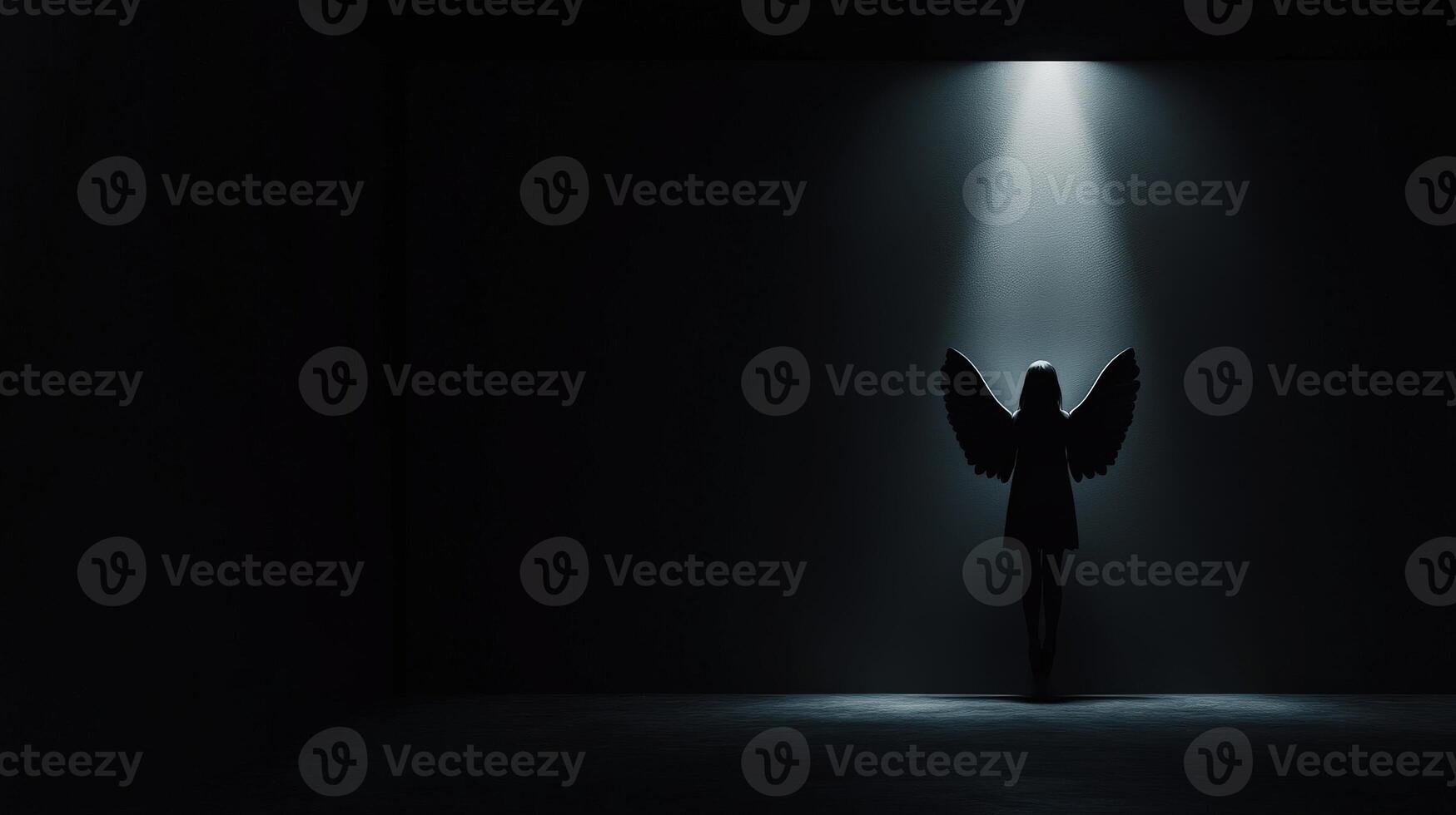 Silhouette of a figure with wings illuminated in a dark space photo