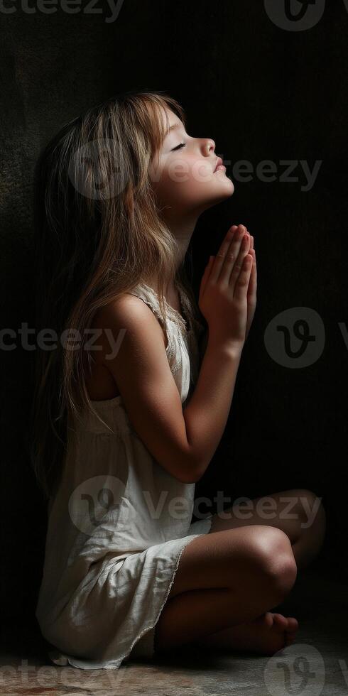 Child in prayer with closed eyes in a dimly lit room photo