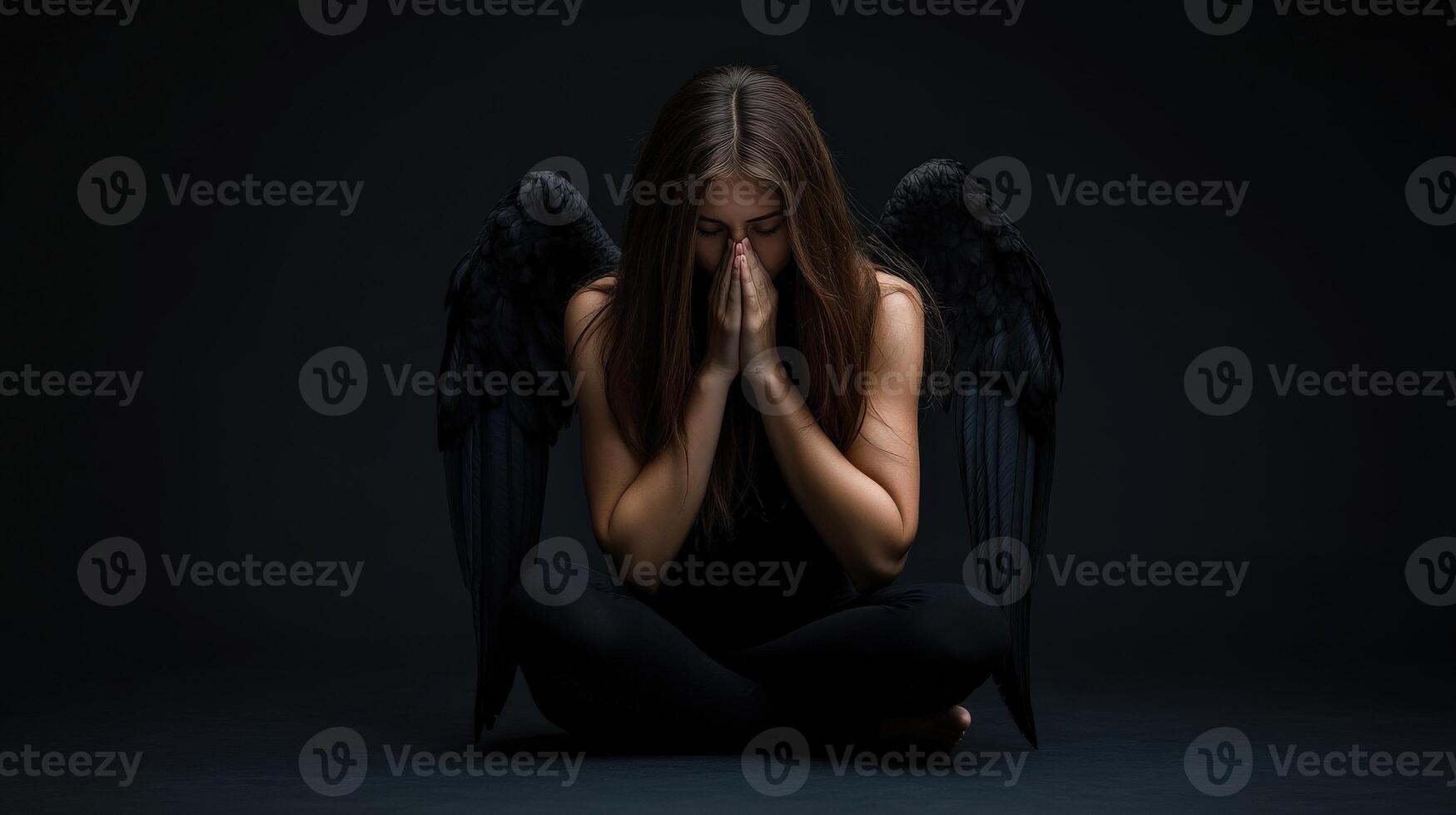 Dark angel sitting in contemplation with folded hands in a dimly lit space photo