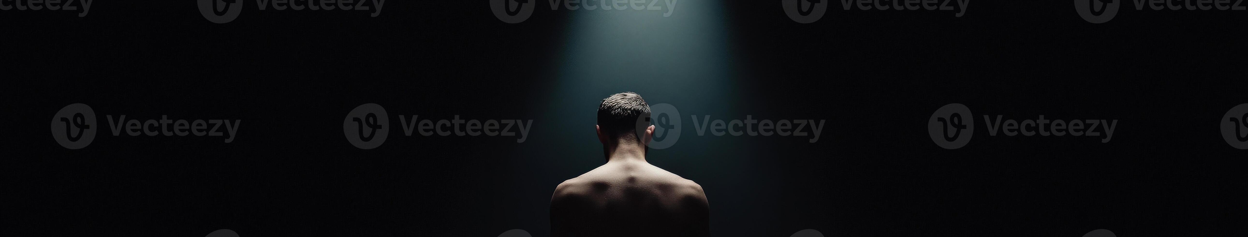 Man under a spotlight in a dark space during a moment of introspection photo