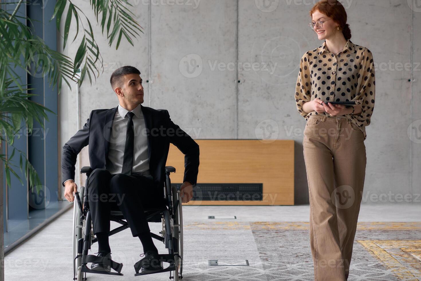 Director in a Wheelchair Engaging in a Business Discussion with a Colleague While Navigating a Modern Office photo
