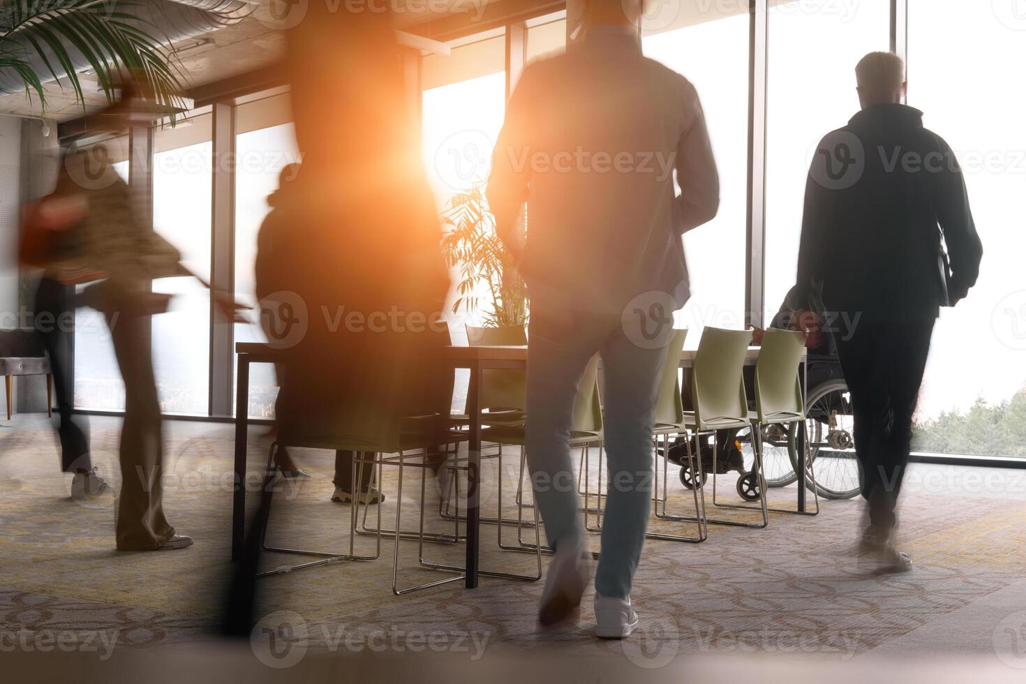 A diverse business team, working urgently around a conference table, collaborates on a meeting while their director, seated in a wheelchair, waits for their input photo