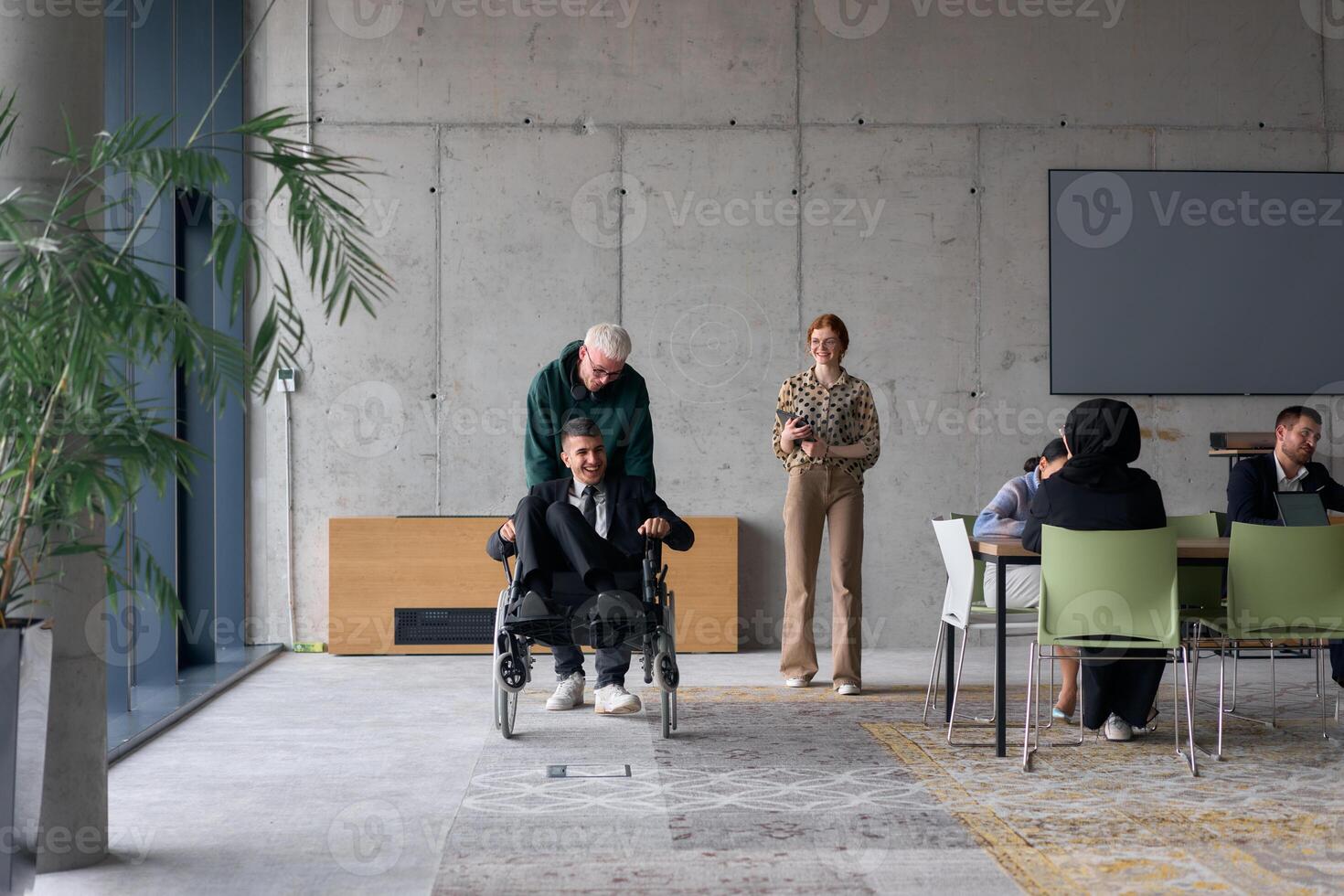 A diverse team of business colleagues, including a director in a wheelchair, engages in a collaborative discussion as they move together through a modern office space photo