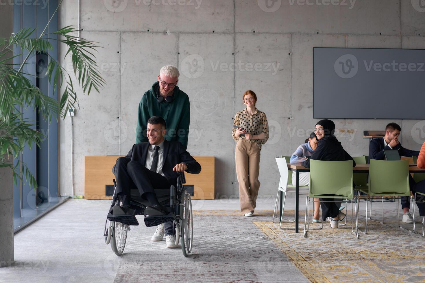 A diverse team of business colleagues, including a director in a wheelchair, engages in a collaborative discussion as they move together through a modern office space photo