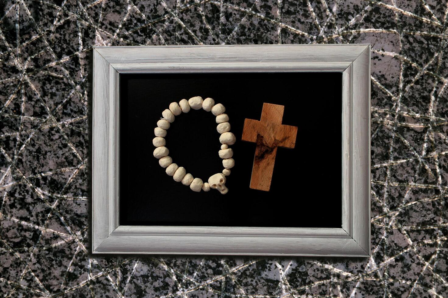 Beads with a white skull and a cross made of rough-textured wood on a black background. White frame photo