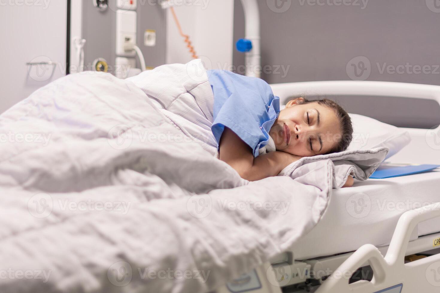 Young female patient of the clinic in blue robe sleeping on hospital bed in calm environment in private room, soft lighting, concept of recovery and care, copy space photo