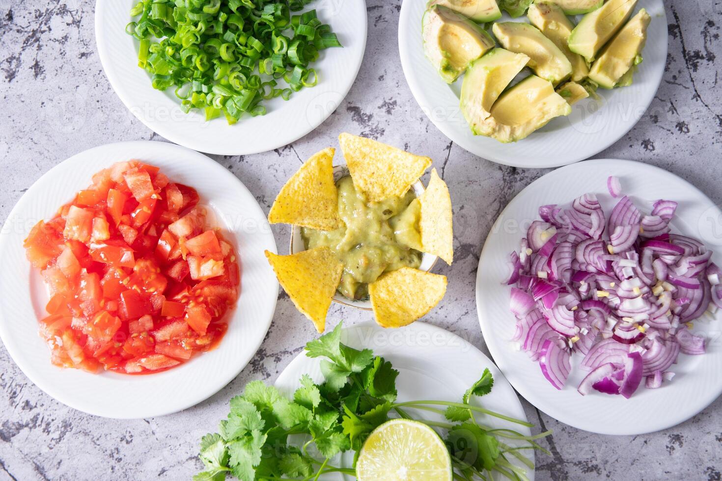 Freshly prepared Mexican snack guacamole, avocado, tomatoes, onions, cilantro and lime on white plates on marble table background, top view photo