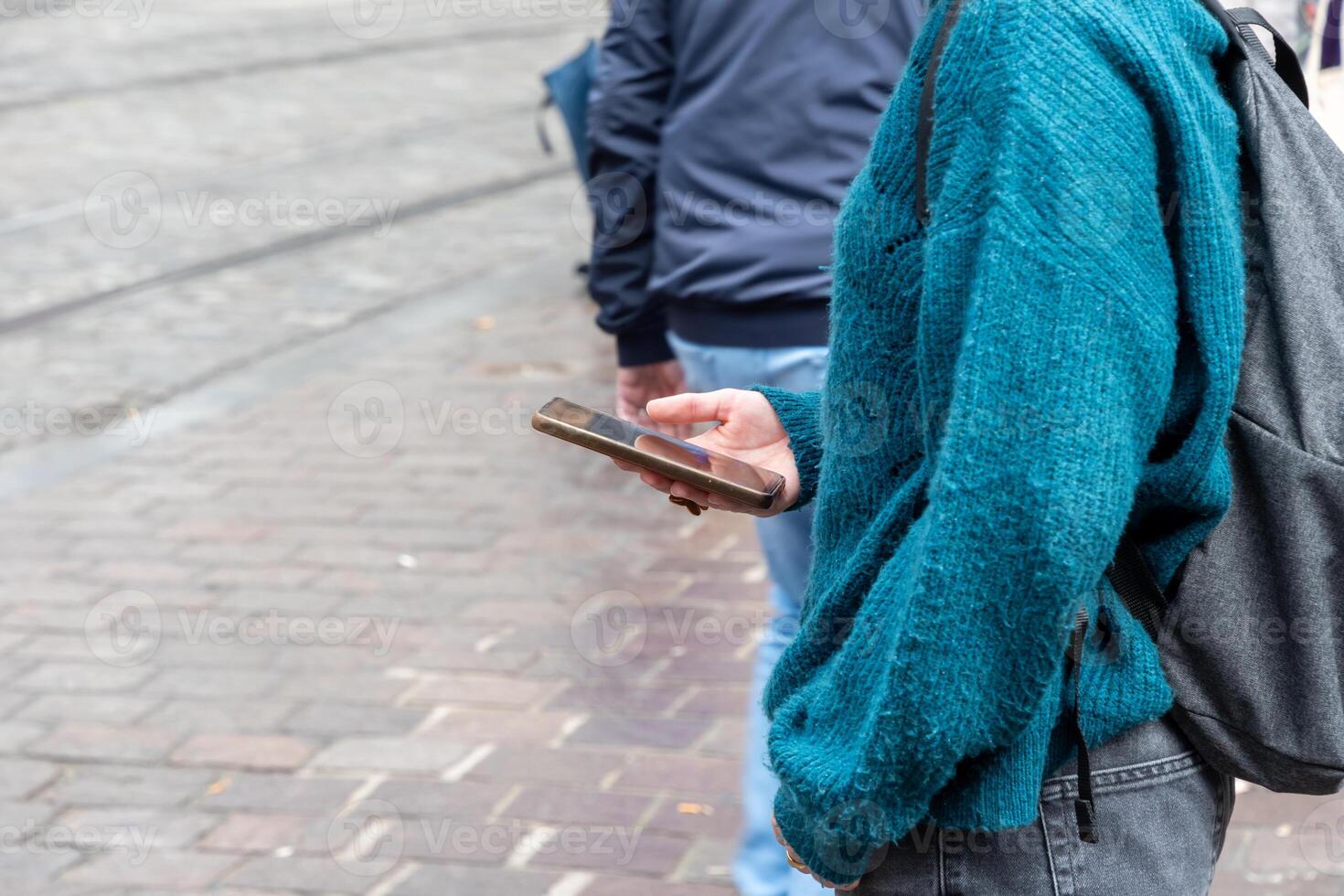 young unrecognizable student girl in blue sweater using smartphone while waiting for bus at bus stop in city, unlimited internet access, photo