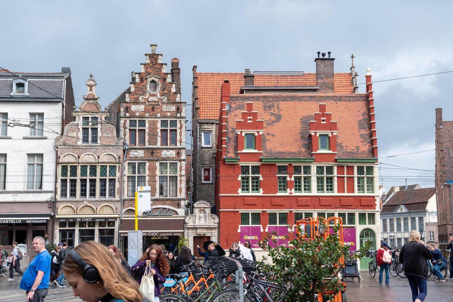 Scenic view of beautiful historic brick building with traditional architecture, cyclist riding on street among pedestrians and cars after rain, Ghent, Belgium, September 24, 2024, photo
