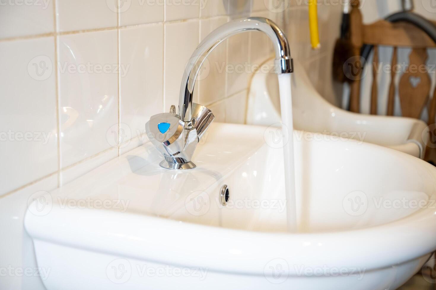 Flowing water from a shiny chrome faucet into a white sink, tiled wall background, clean and modern design concept, photo