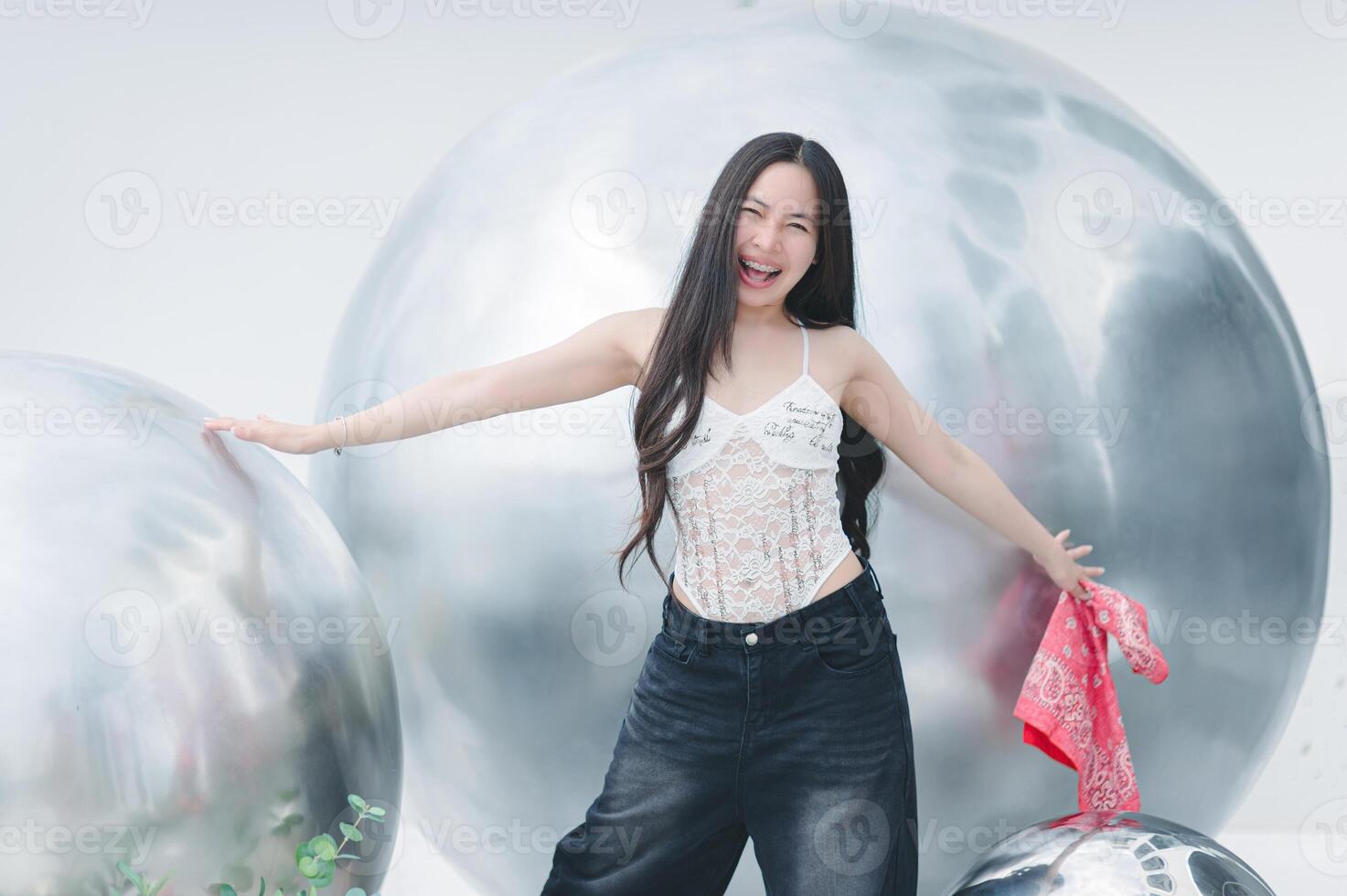 A woman in a white top and jeans is posing in front of large silver balls photo