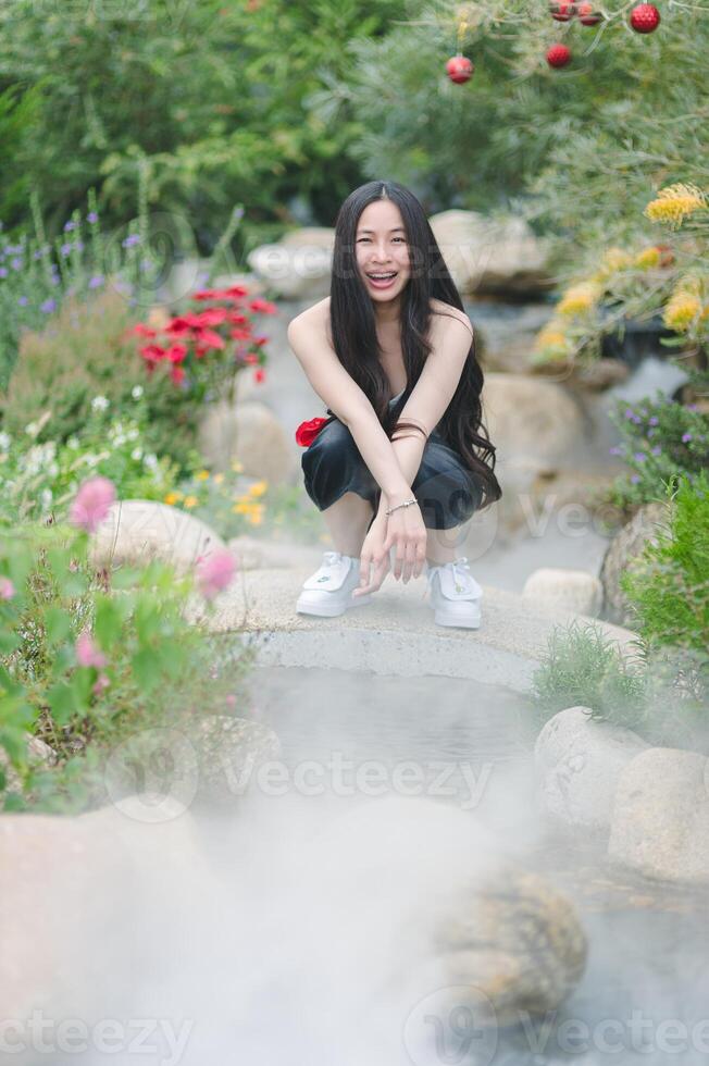 A woman in white sneakers crouches on a stone bridge in a garden photo
