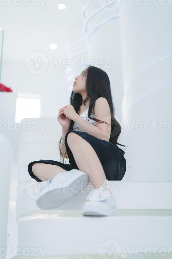 Young Woman Sitting on White Spiral Stairs in Bright Interior Space photo