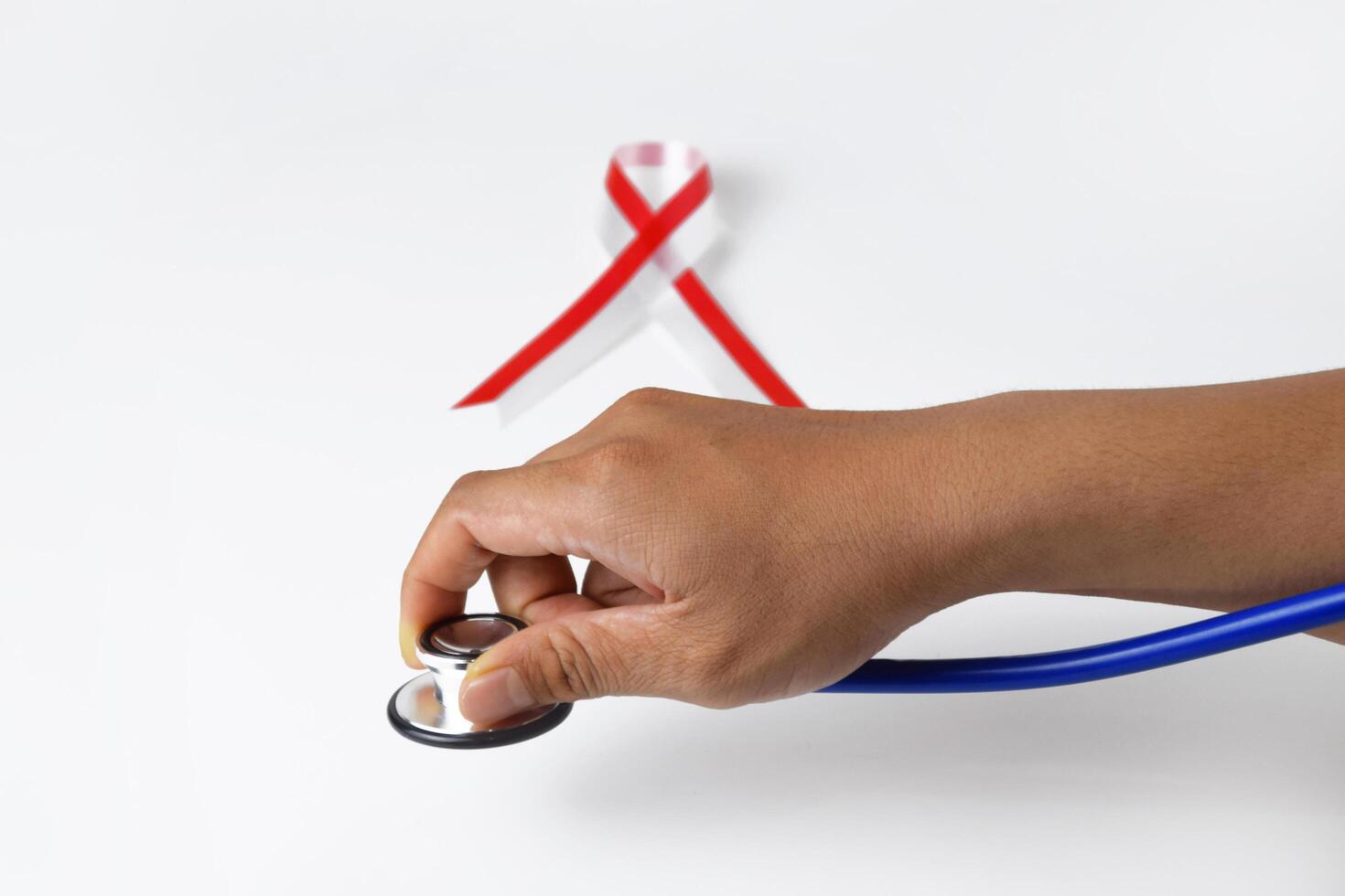 People's hands holding a Stethoscope with a red and white ribbon photo