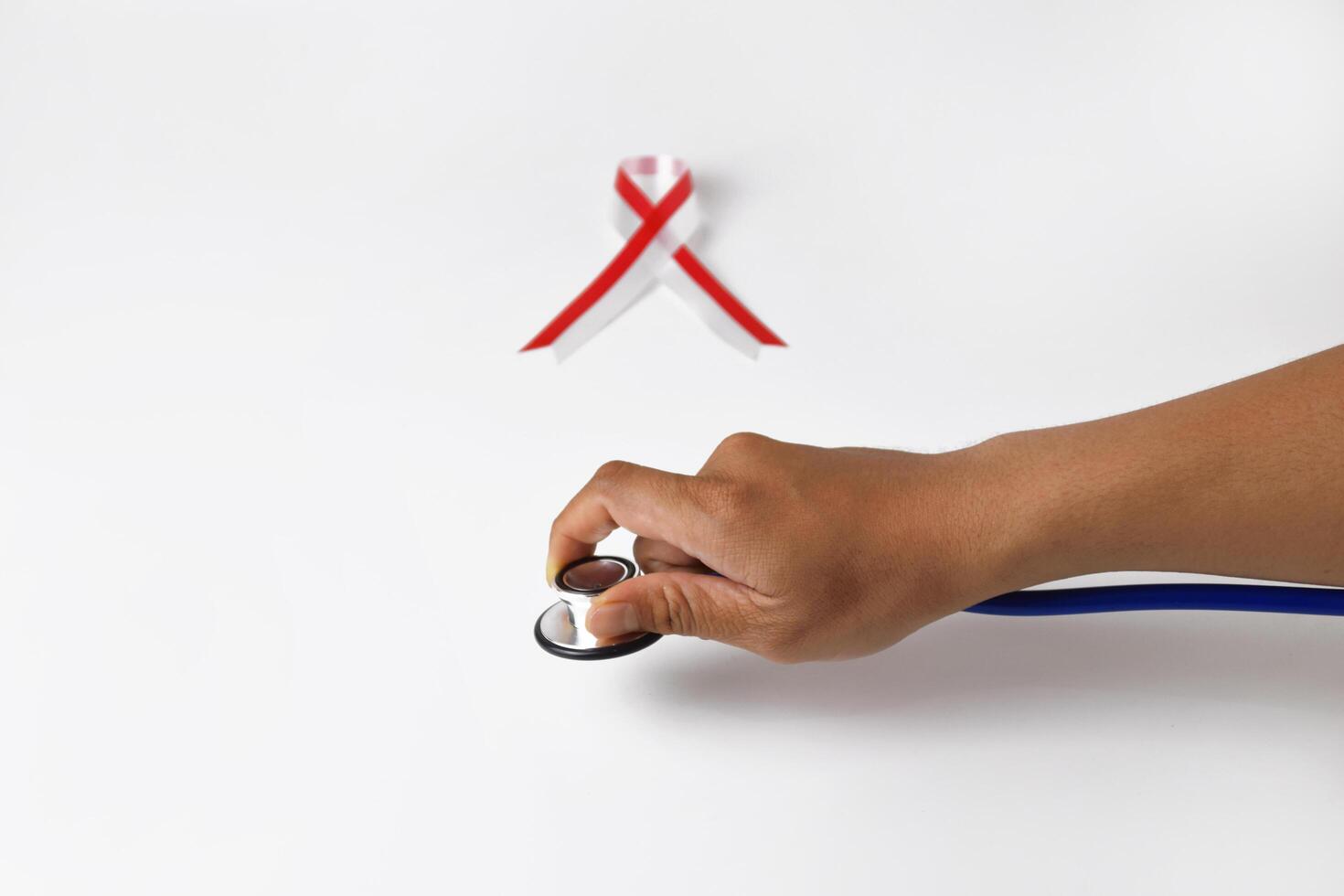 A person's hand holding a Stethoscope with a red and white ribbon photo