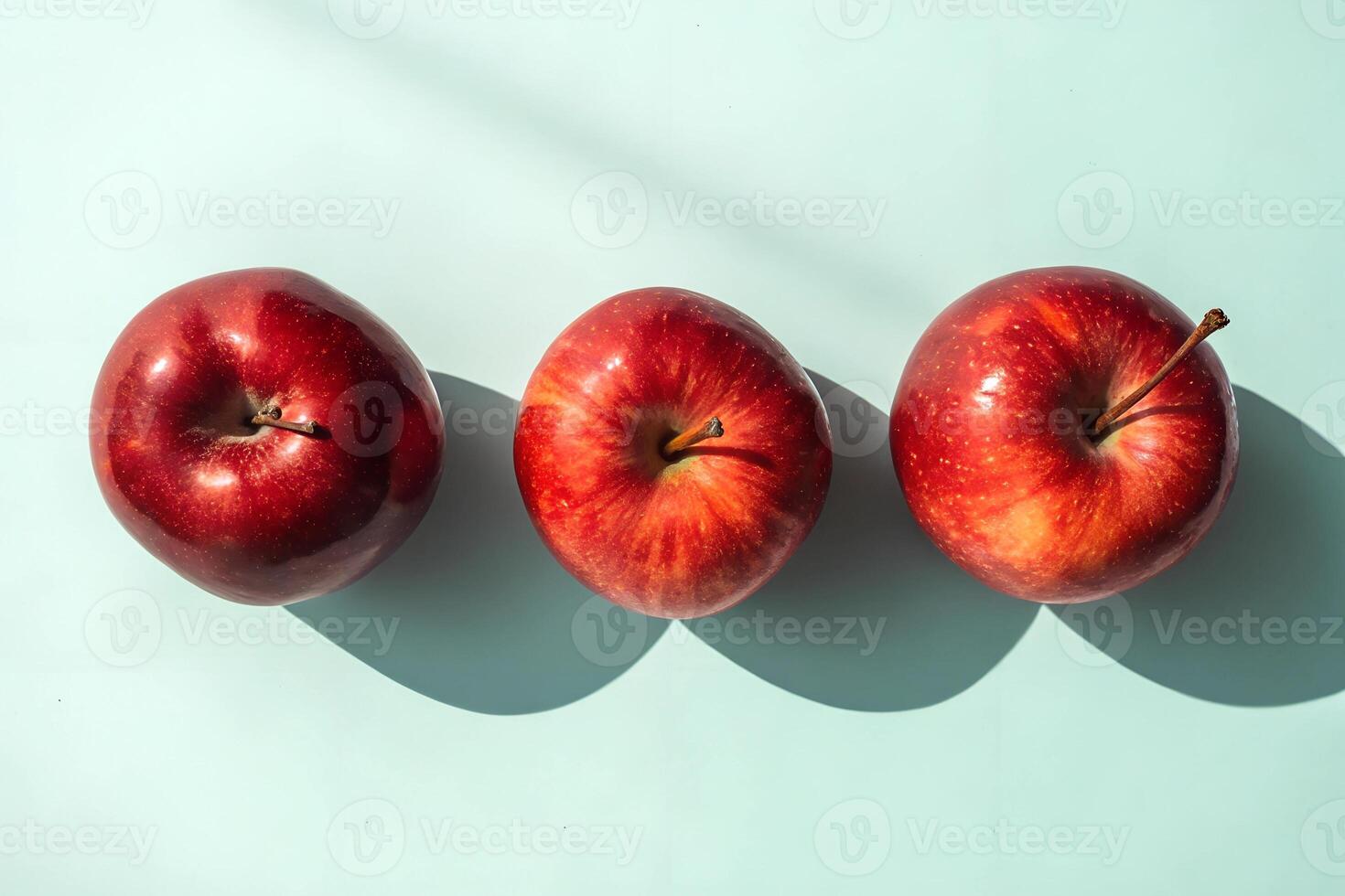 Fresh red apples arranged in a row on a light blue background casting soft shadows in bright sunlight photo