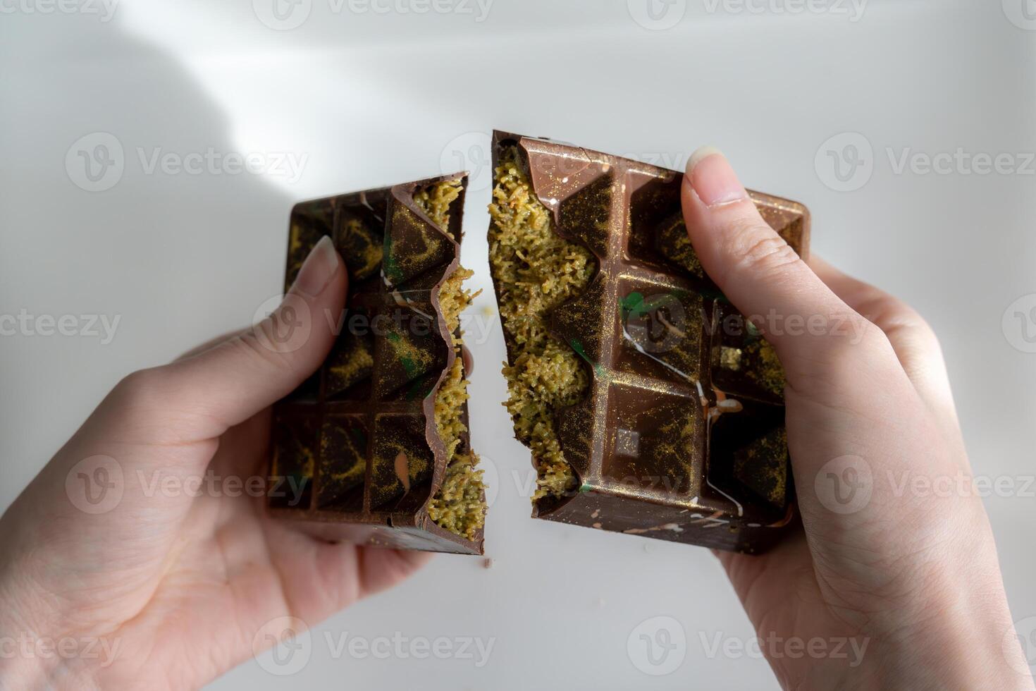 Trend Dubai chocolate with pistachio, tahini and kataifi dough, chocolate broken in woman's hands. Handmade confectionary photo