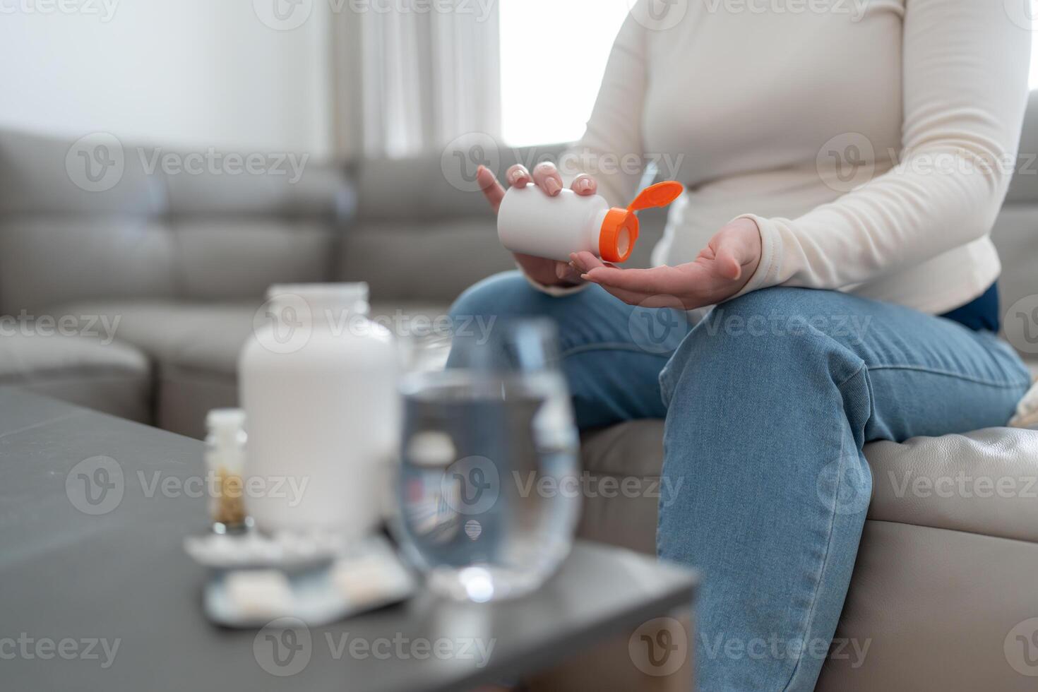 Unrecognizable pregnant woman holding jar with pills taking vitamins and minerals treating sickness during pregnancy sitting on sofa at home. Pregnancy, health, pharmaceuticals concept. photo