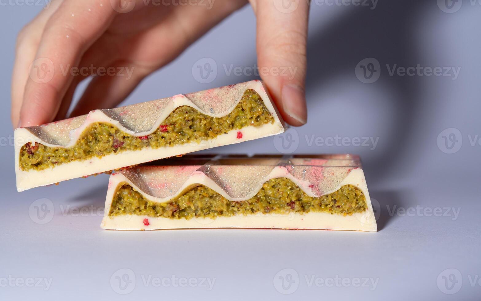 Trend white Dubai chocolate with pistachio, dried raspberry, tahini and kadaif, isolated, showing the filling. Chocolate in woman hands. Close up. Confectionery and handmade sweets, chocolatier photo