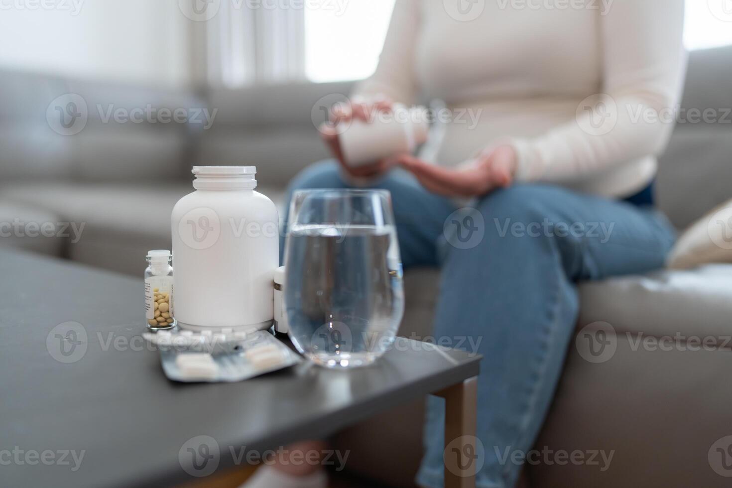 Unrecognizable anonymous pregnant woman holding jar with pills taking vitamins and minerals treating sickness during pregnancy sitting on sofa at home photo