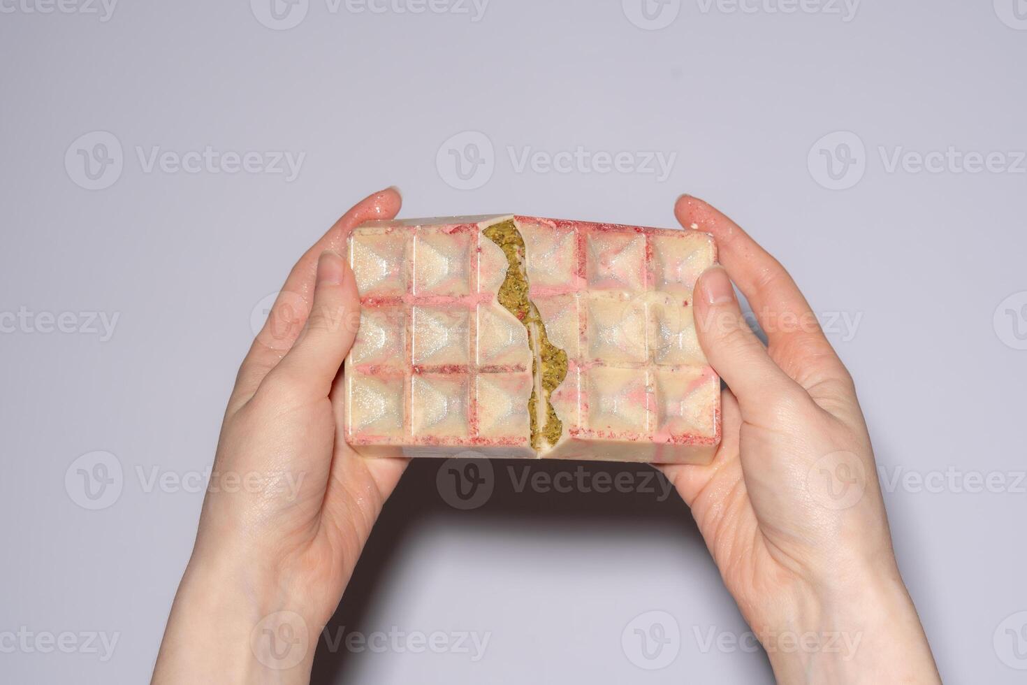 Popular white Dubai chocolate with pistachio, dried raspberry, tahini and kadaif filling, chocolate broken in woman's hands. Confectionery and handmade sweets, chocolatier photo