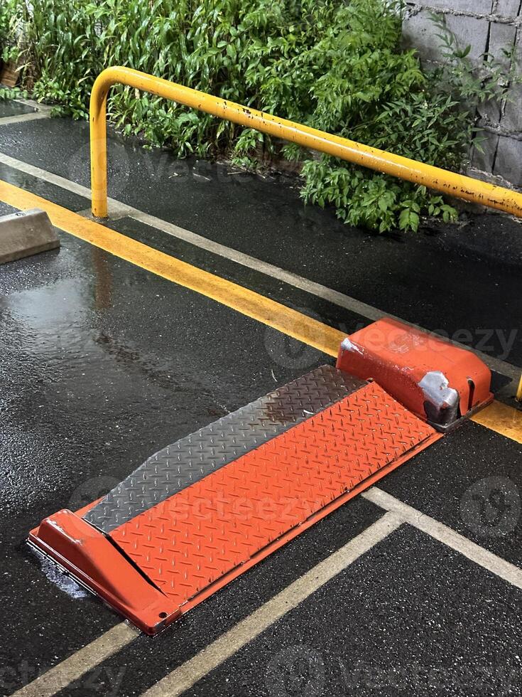 Wet parking lot barrier with reflective orange ramp. Concept of traffic management, urban infrastructure, and safety measures. photo