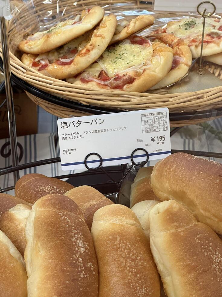 Kyoto, Japan - May 25, 2024. Freshly baked salted butter rolls and mini pizzas on display in Japanese bakery. Concept of bakery delights, Japanese cuisine, and appetizing comfort food. photo