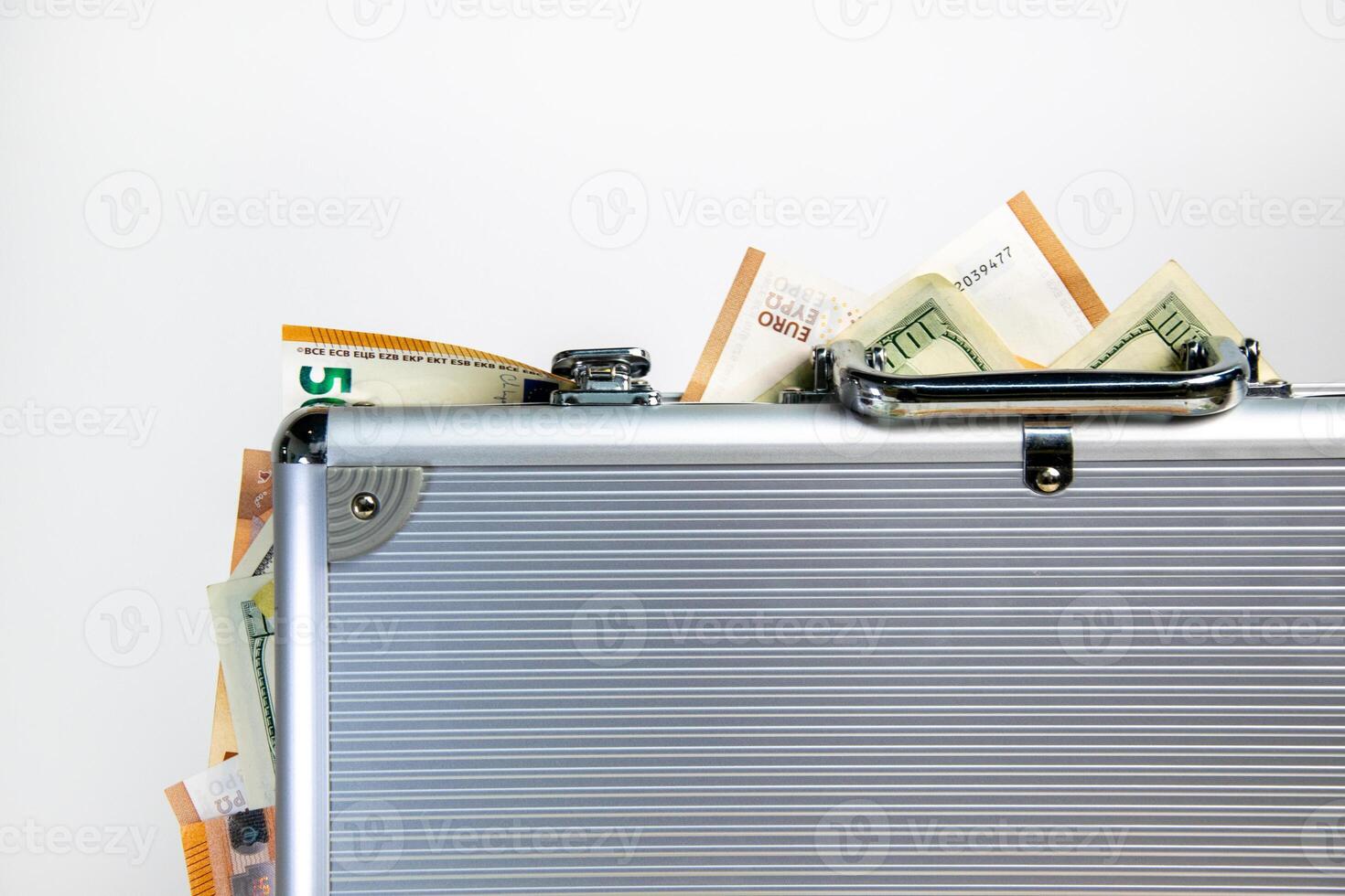 A silver metal briefcase sits closed with US dollar and euro bills partially visible inside photo