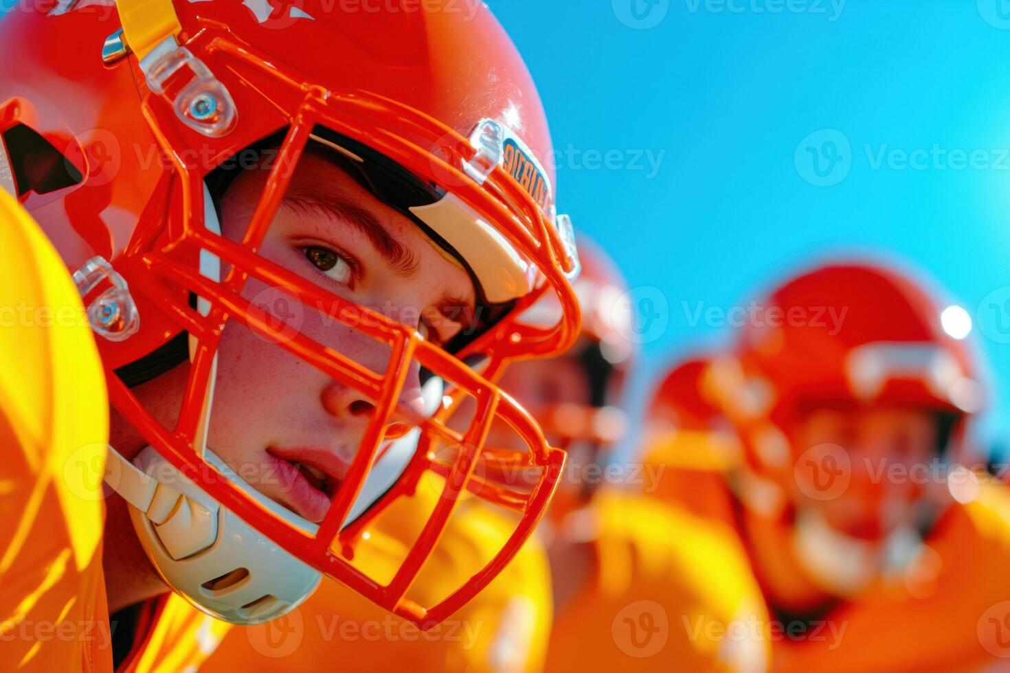 Dynamic outdoor football game featuring players in orange and yellow uniforms under a clear blue sky photo