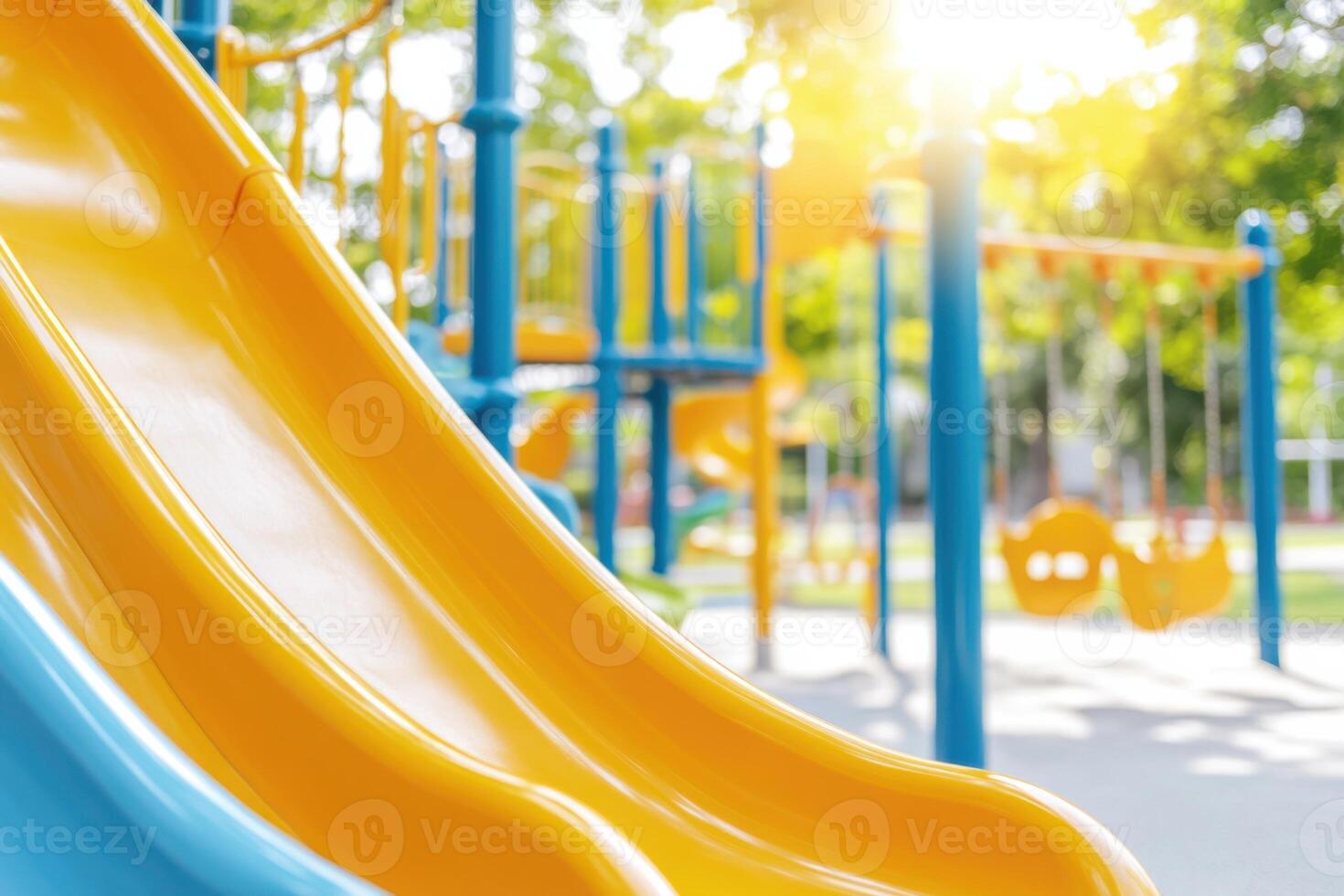Whimsical playground for children featuring yellow slides and swings surrounded by green trees under bright sunlight photo