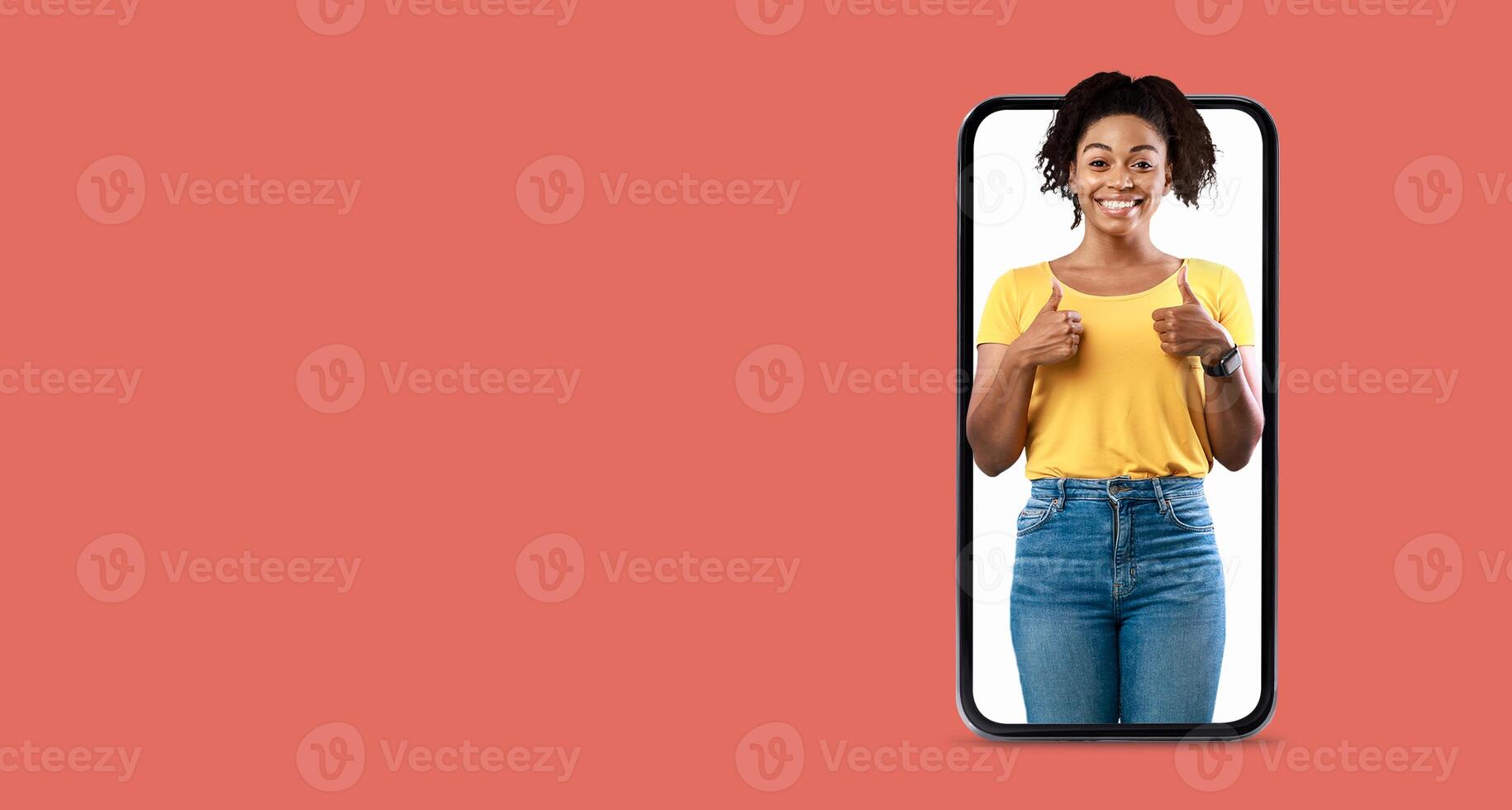 A person is smiling and giving a thumbs up gesture while interacting with a large smartphone. The background is a solid color, emphasizing their joyful expression and the technology. photo