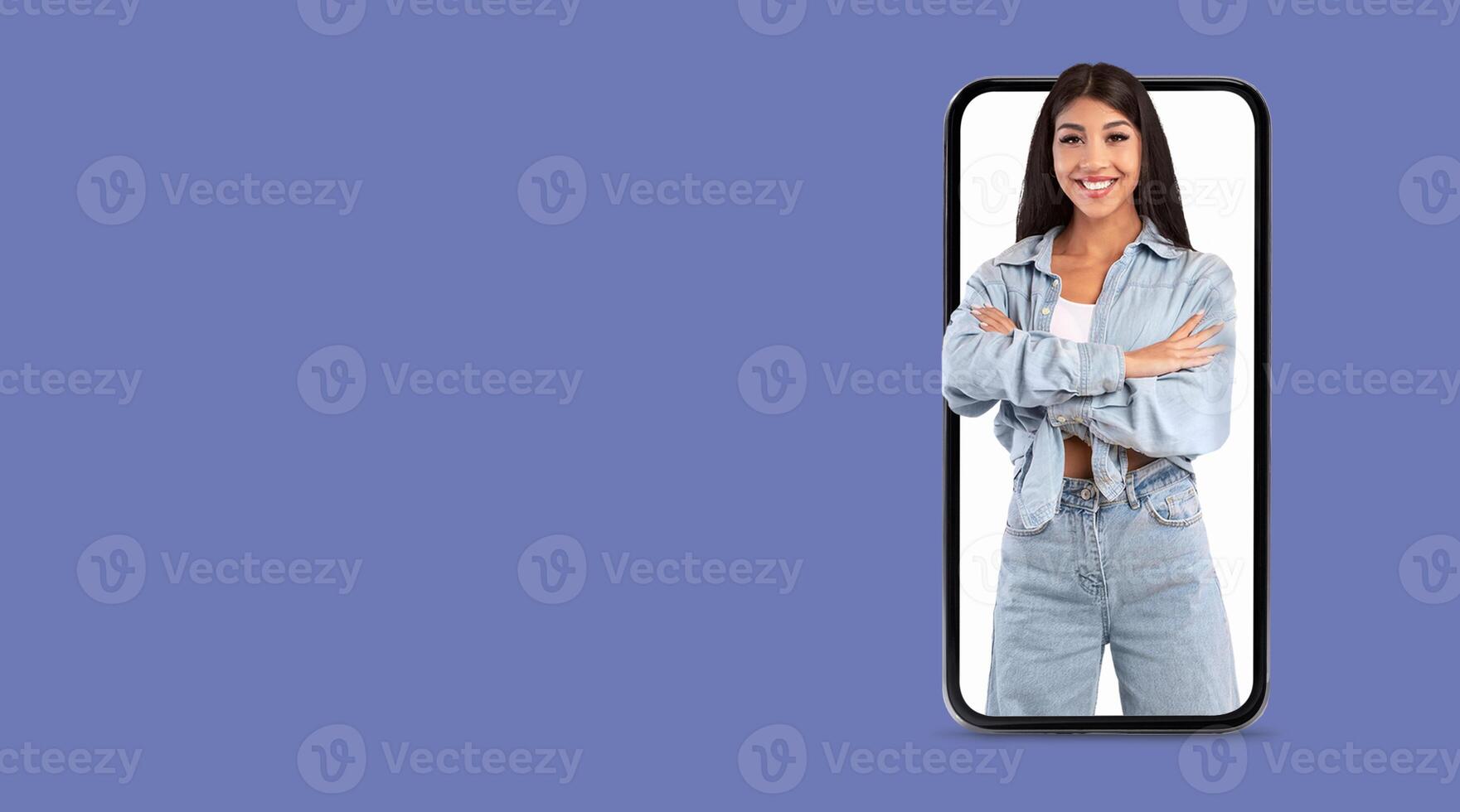 A person smiles confidently, standing with arms crossed in front of a large smartphone screen. This depicts modern communication and social media engagement in a technology-focused environment. photo