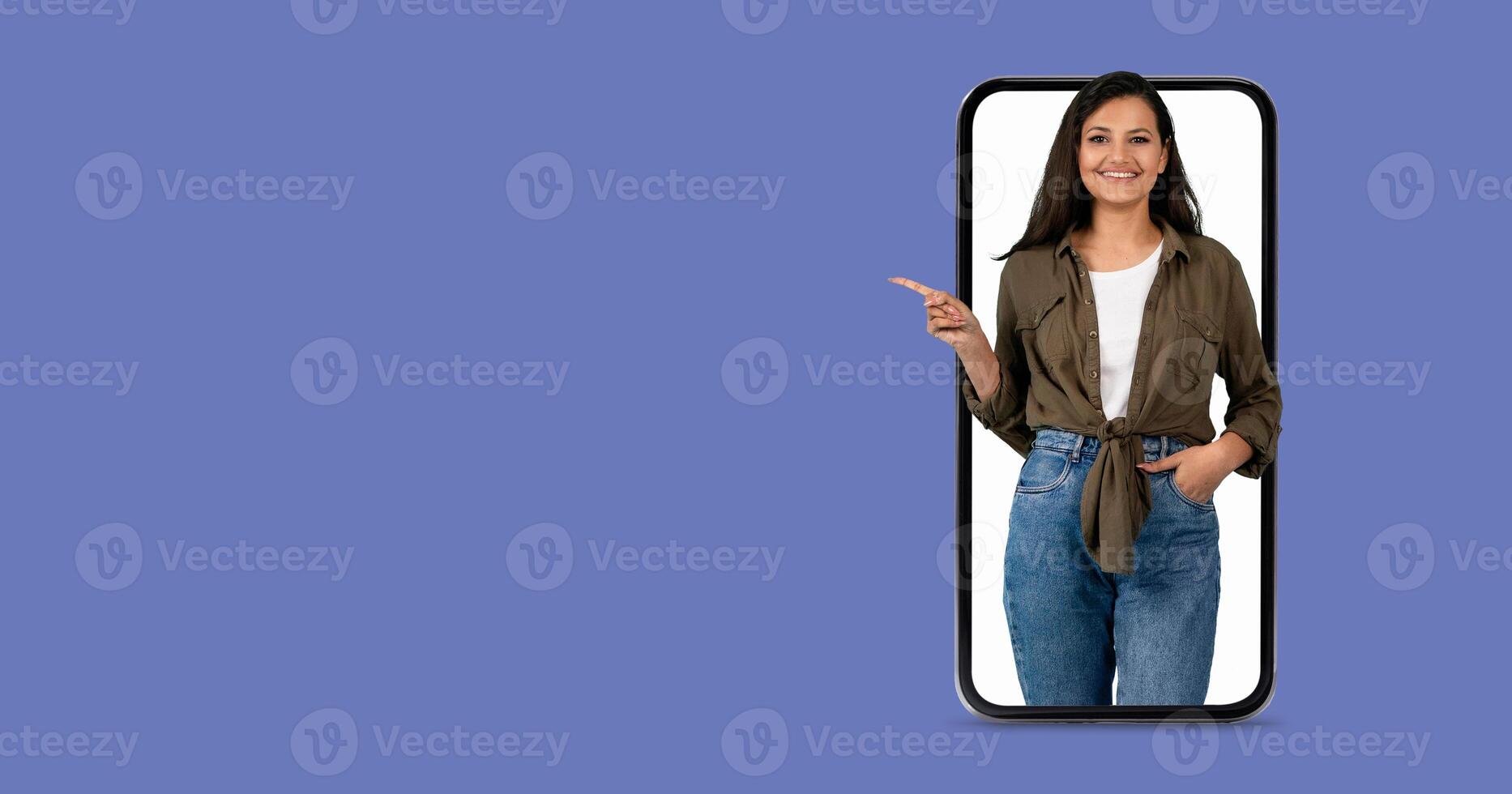A woman with a friendly expression is interacting with a large smartphone. She points towards the screen while showcasing the engaging communication features of modern technology. photo