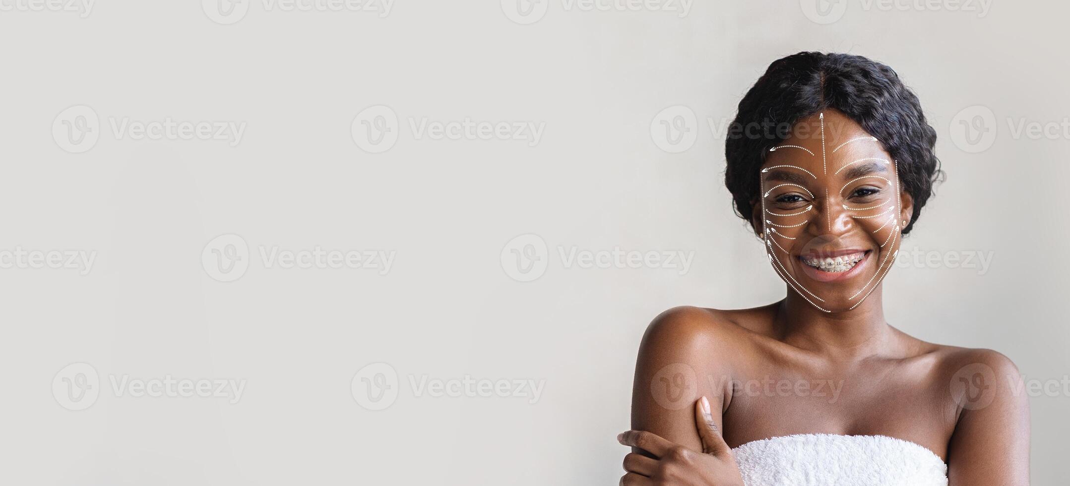 African American woman is applying a facial mask while showcasing her clear skin and happy expression. She is isolated against a plain background photo