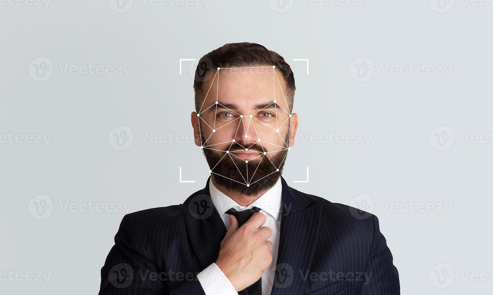 A suited man adjusts his tie as facial recognition technology highlights his features for identification purposes. The empty background emphasizes the focus on the subject's face and expression. photo