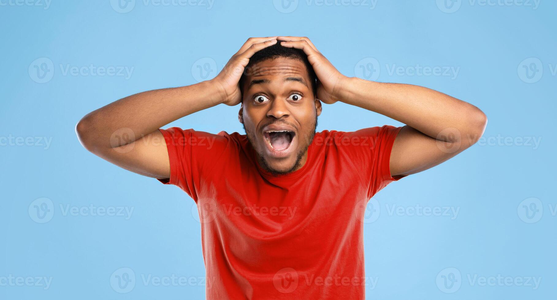 Omg. Shocked African American Guy Shouting Looking At Camera In Shock Posing Touching Head Standing Over Blue Studio Background, Wearing Bright Yellow T-Shirt. Shocking News, Amazement Concept photo