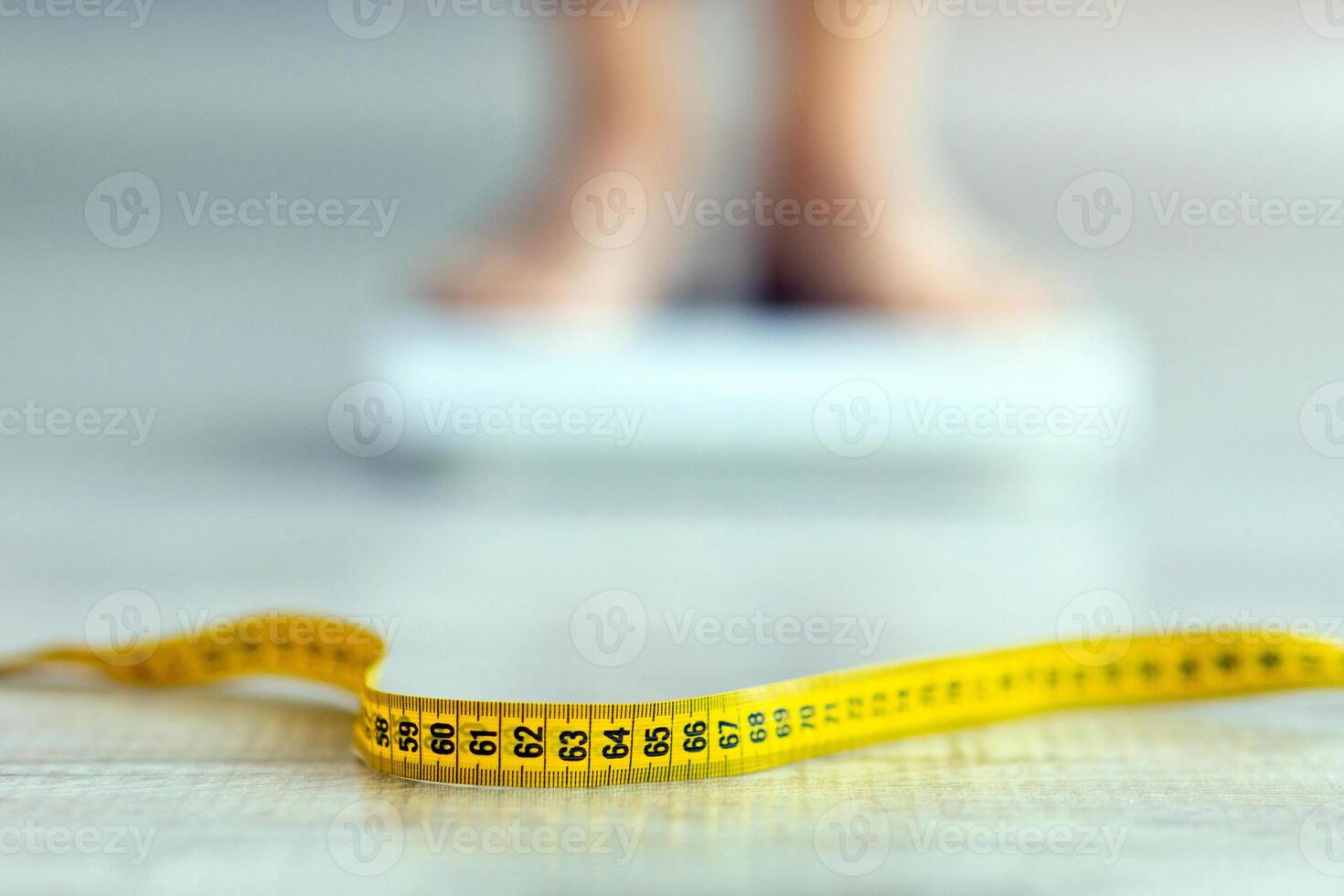 Measuring tape on floor and blurred view of millennial woman on scales, checking result of her slimming diet, selective focus. Healthy living, weight control concept. Copy space photo