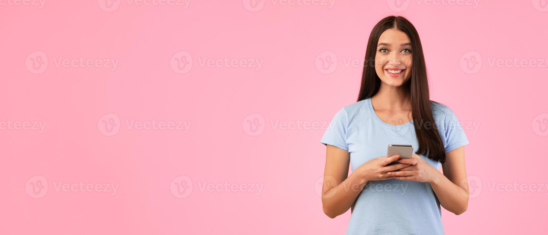 People And Technology Concept. Portrait of happy smiling young woman using smartphone standing isolated over yellow studio background, copy space. Lady chatting online, looking at camera photo