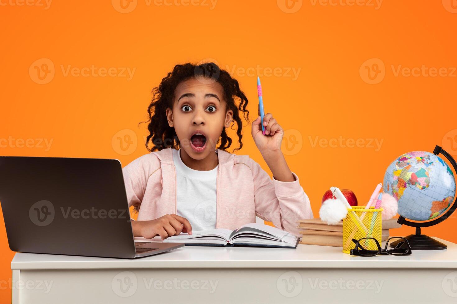 Idea Concept. Excited Young Black Pupil Sitting At The Desk Using Laptop And Raising Pen Up Isolated Over Yellow Orange Background In Studio. Amazed Shocked Girl Having Insight, Aha Moment. photo