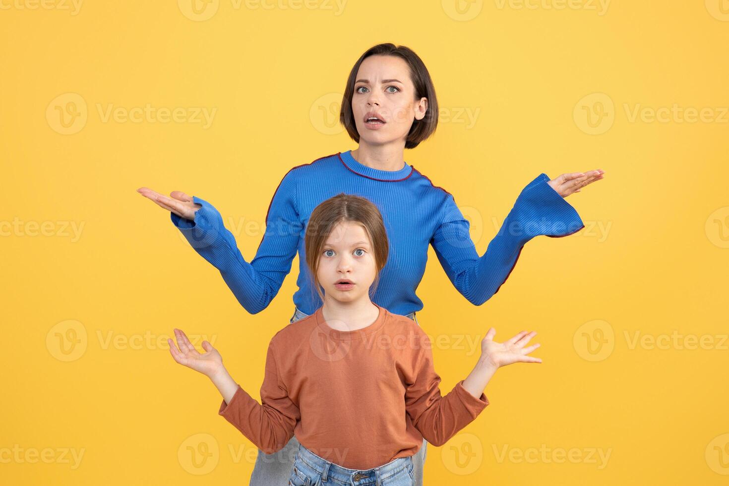 A mother and her preteen daughter display a moment of shared confusion and surprise against a bright yellow background. They both express emotions of bewilderment together. photo