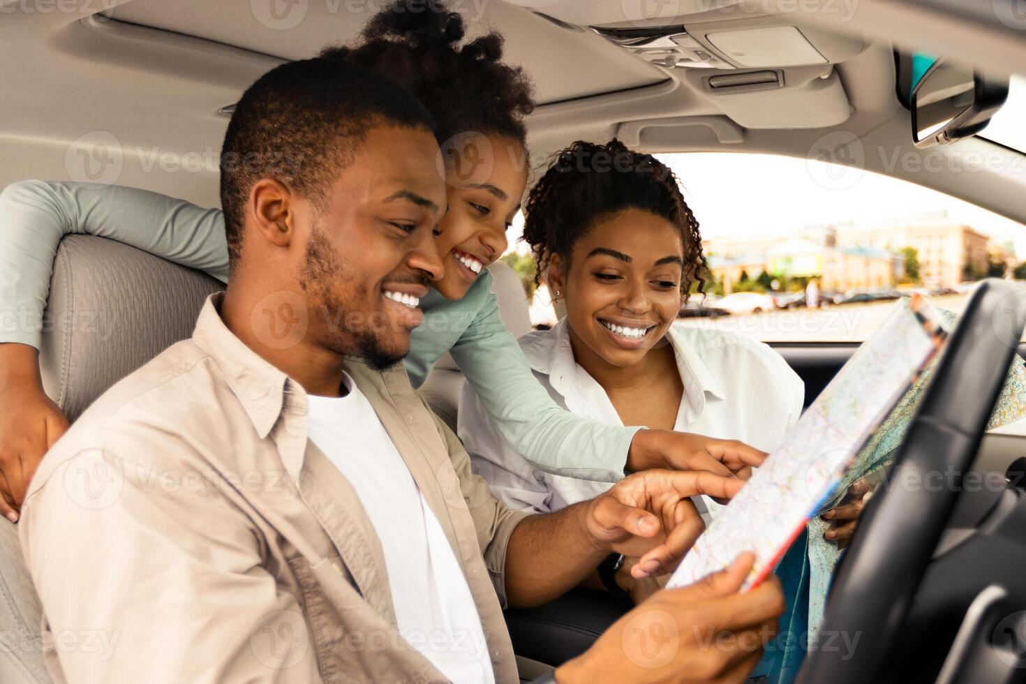 Road Trip Adventure. Happy African American Family Holding Map Sitting In Car Choosing Destination For Vacation. Travel By Automobile. Transportation And Navigation. Selective Focus, Side View photo