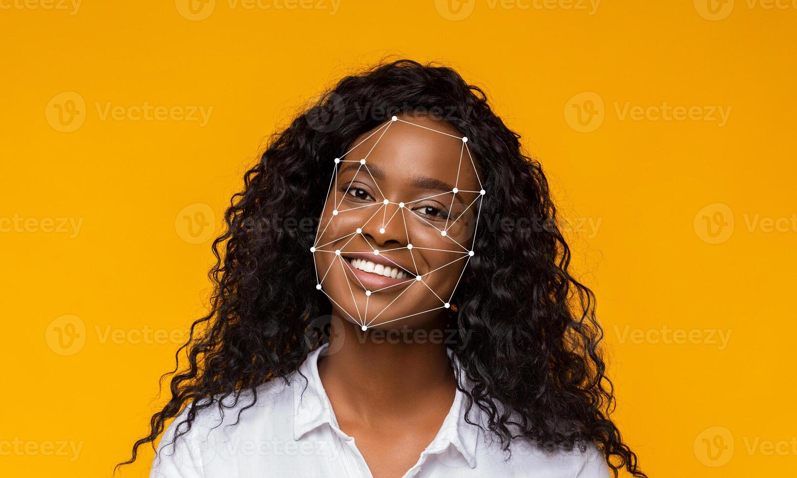 A woman with curly hair smiles brightly, while facial recognition markers overlay her face. The vibrant yellow background enhances the focus on her joyful expression and the technology used. photo