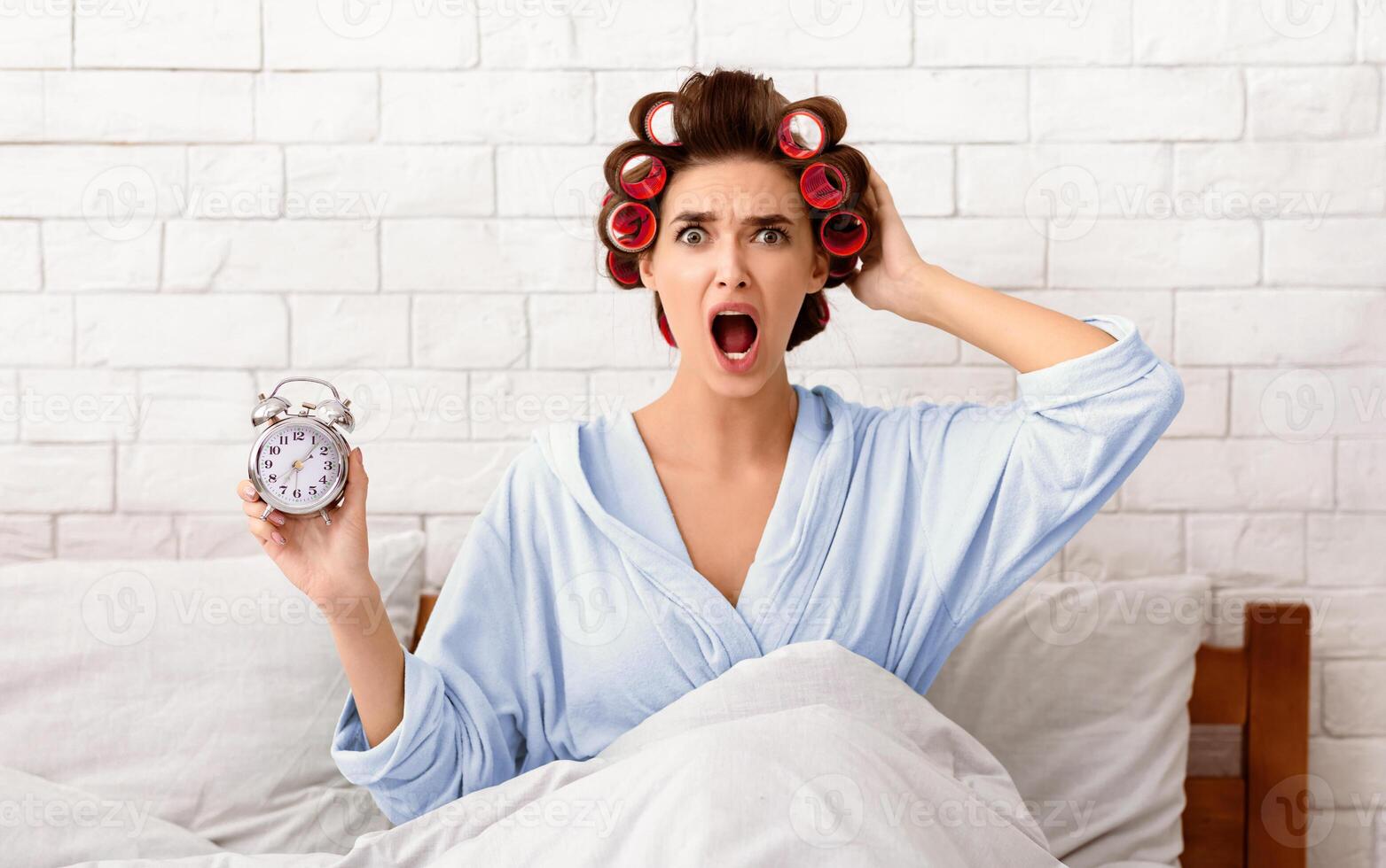 Overslept Girl Holding Alarm Clock Sitting In Bed At Home Being Late For Work In The Morning. Oversleeping Concept photo
