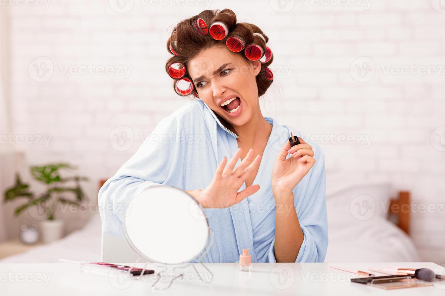 Housewife's Lifestyle. Woman With Curlers Talking On Phone Doing Nails Sitting In Bed At Home. Selective Focus photo