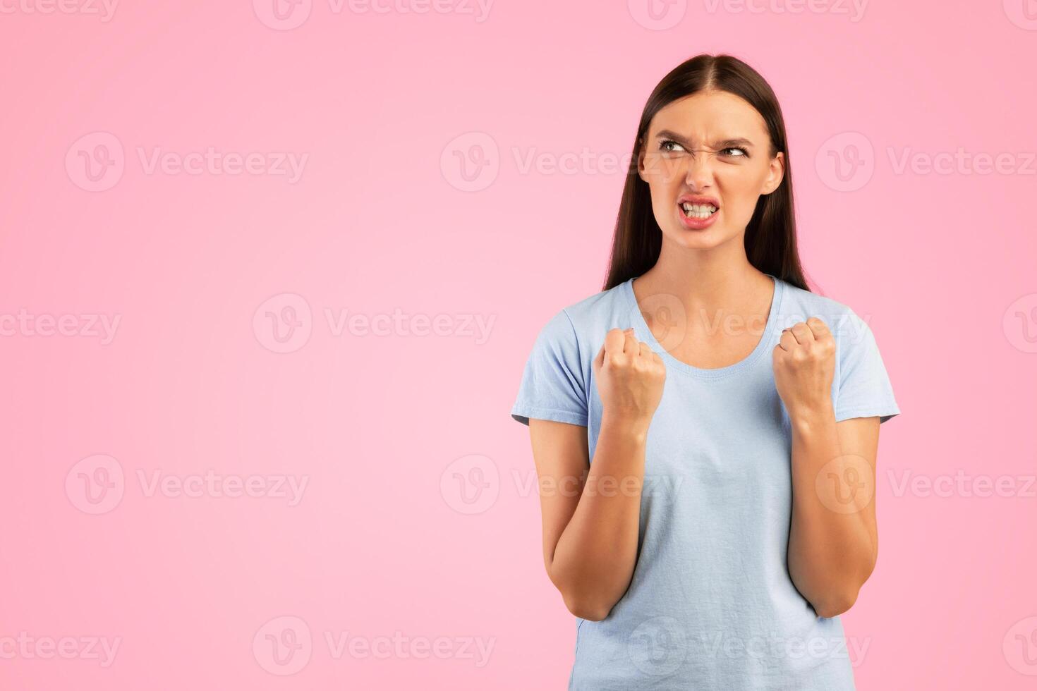 Emotions, Stress, Madness and People Concept. Crazy angry woman holding hands in furious gesture, looking away at copy space. Frustrated lady standing isolated over yellow studio background photo