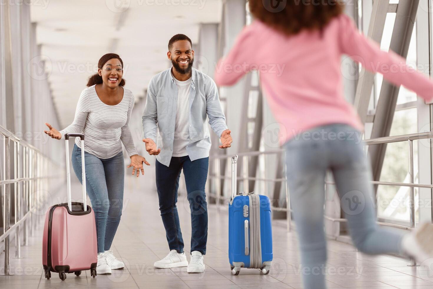 Meeting In Airport. Little black girl running to her parents after arrival in airport, returning back home from vacation journey voyage, happy man and woman ready to embrace their daughter photo