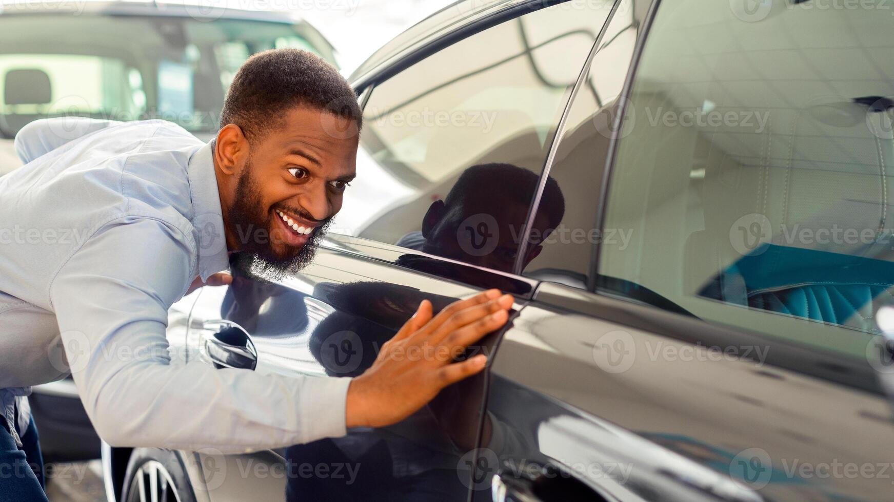 Happy Owner. Excited Black Man Touching His New Car In Showroom After Buying, Overjoyed African American Guy Purchase Automobile In Dealership Salon, Looking At Surface Of New Vehicle, Closeup Shot photo