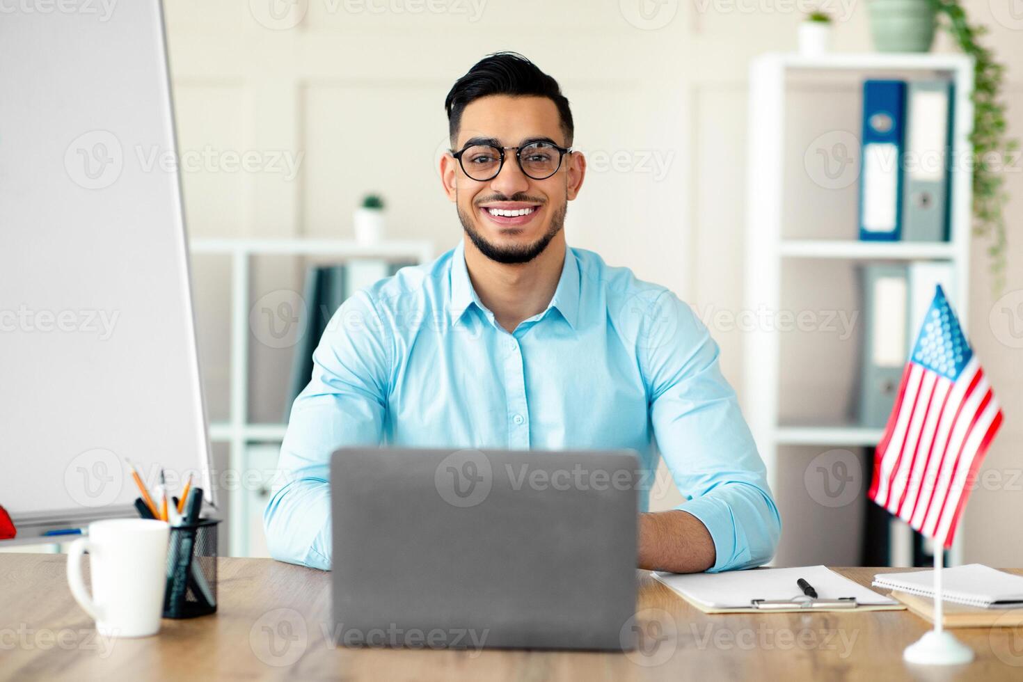 Guy foreign languages tutor teaching English online using laptop at home office. Happy Arab linguistics professor giving remote lesson, communicating to pupils remotely during covid photo