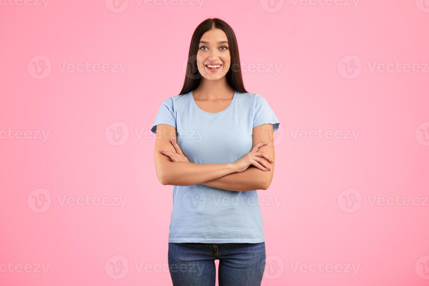 Portrait of happy casual lady smiling, looking at camera and posing with folded arms isolated over yellow studio background. Confident caucasian woman crossing hands, expressing positive emotions photo